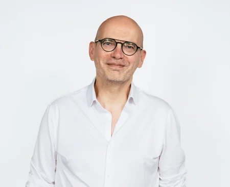 Portrait de Jean-Christophe Le Coustumer, chemise blanche et lunettes, sur fond clair